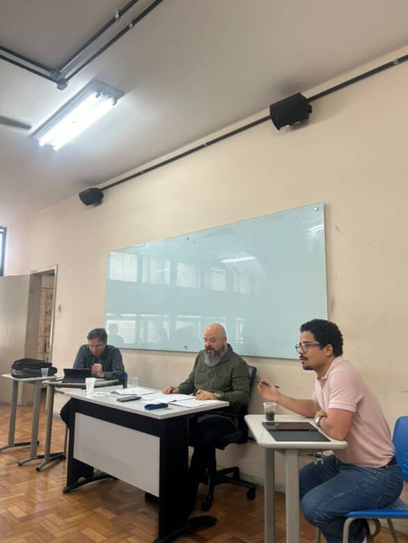 Victor falando numa mesa de apresentação, ao lado de dois outros participantes