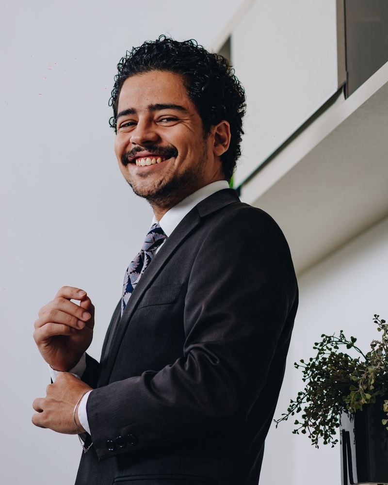Victor Manoel Rangel Soares, sorrindo, de terno escuro, diante de uma estante