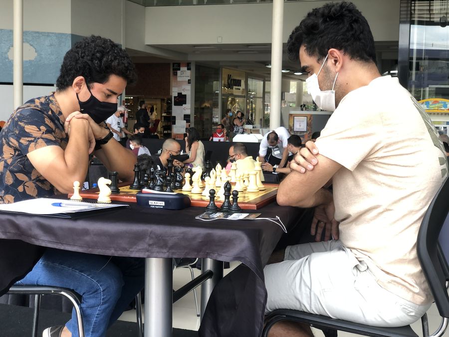 Victor, de máscara, diante de um tabuleiro de xadrez numa partida de torneio